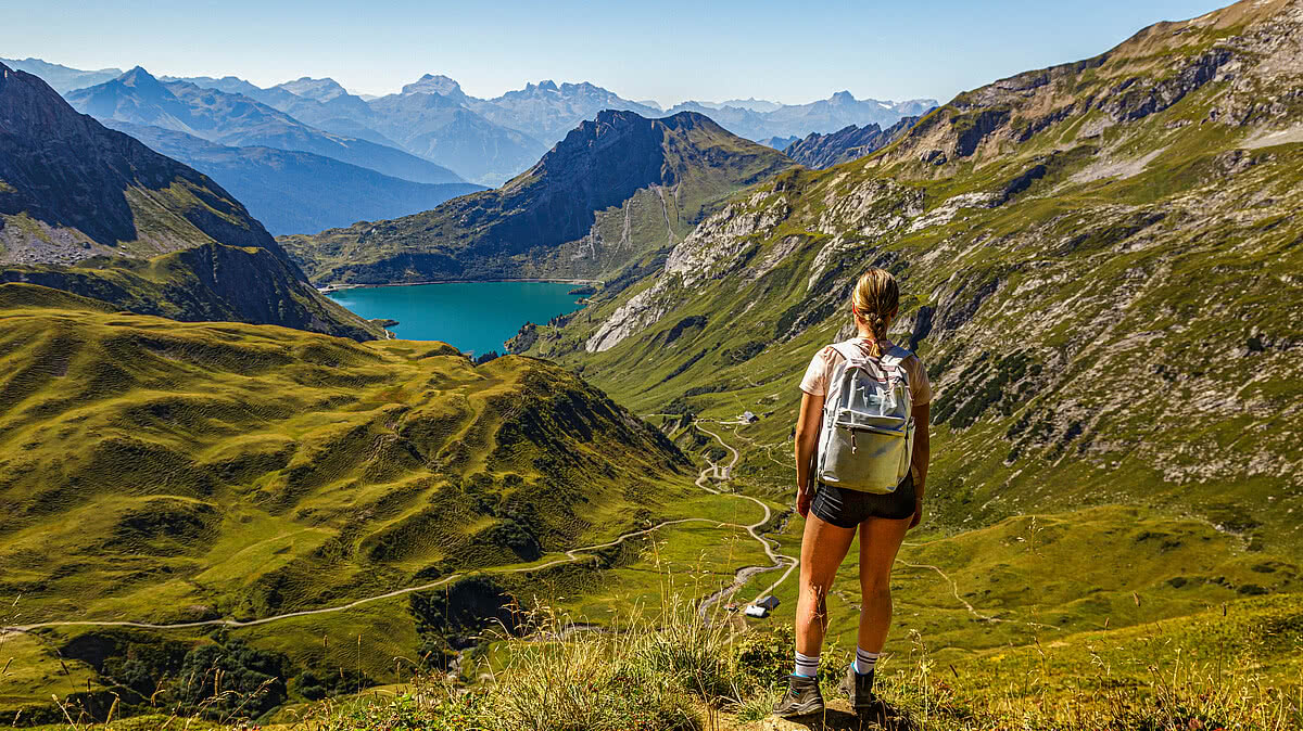 eine junge Frau steht an einem Wanderweg auf einem Berg und schaut auf den Spullersee in Vorarlberg Lech Östereich